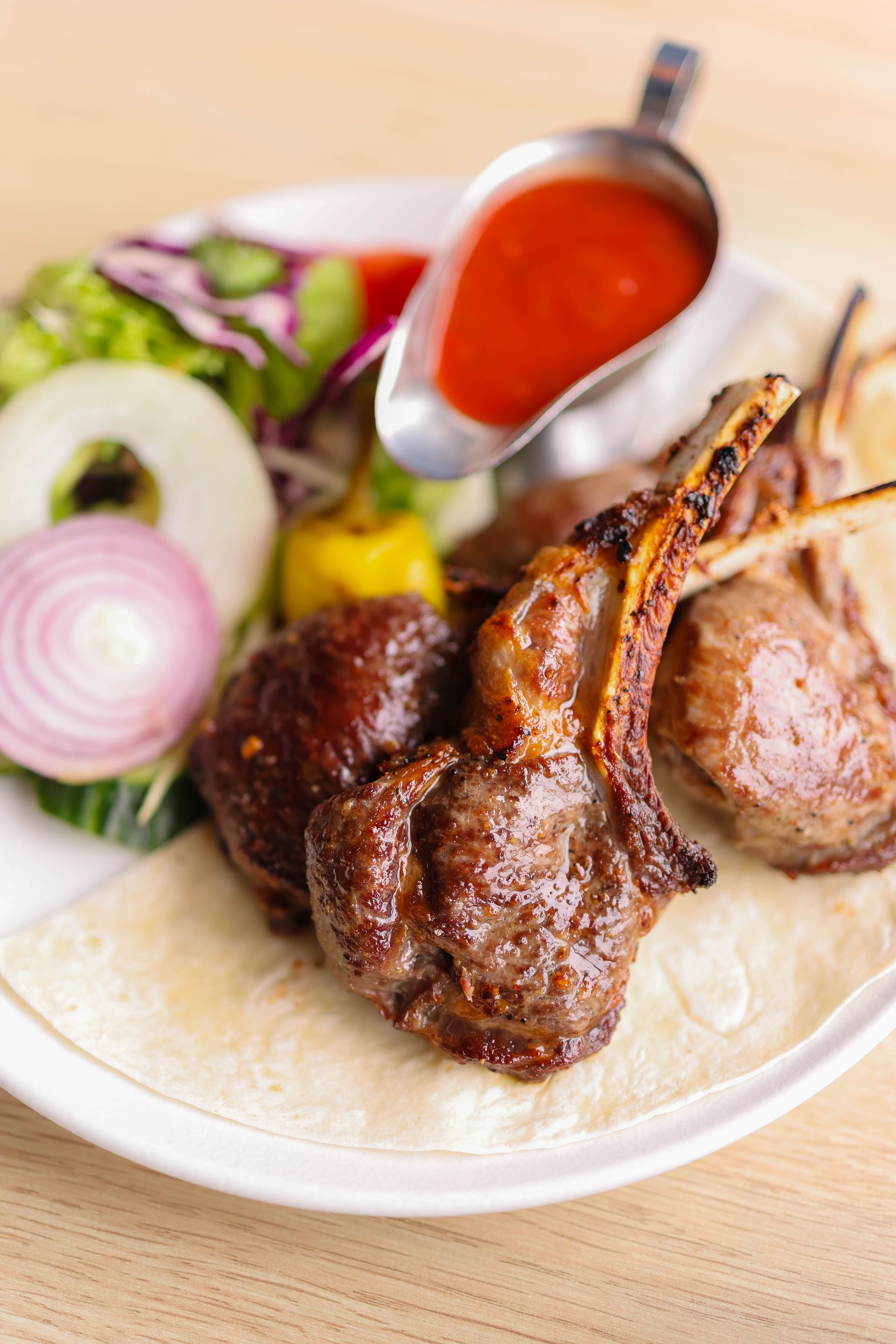Juicy lamb chops on a plate with red sauce, salad, and a side of flatbread.