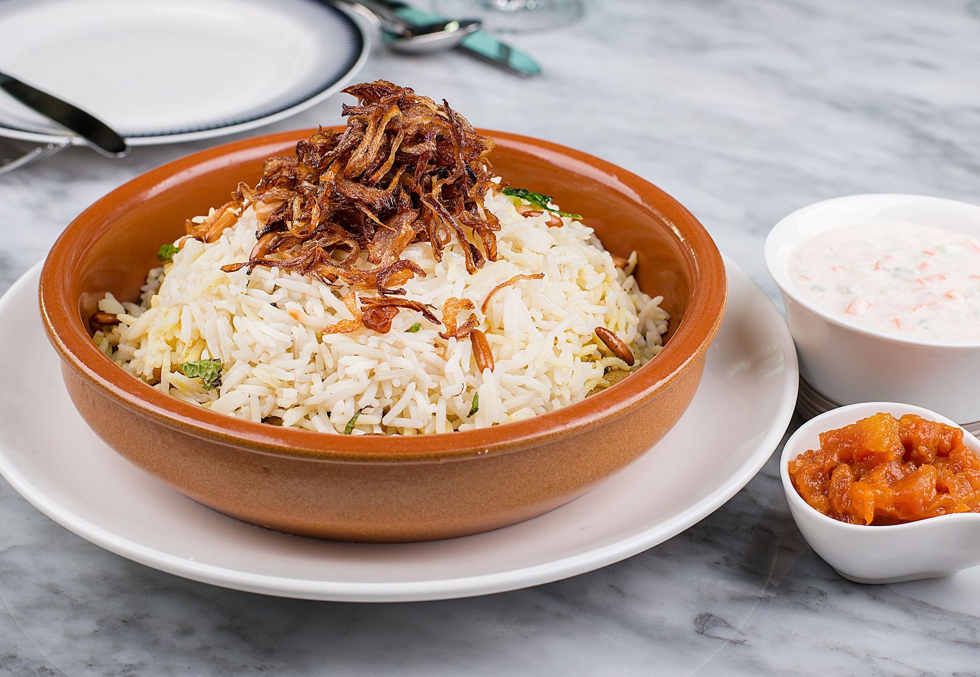 Delicious basmati rice topped with crispy fried onions, served with sides of yogurt and chutney.