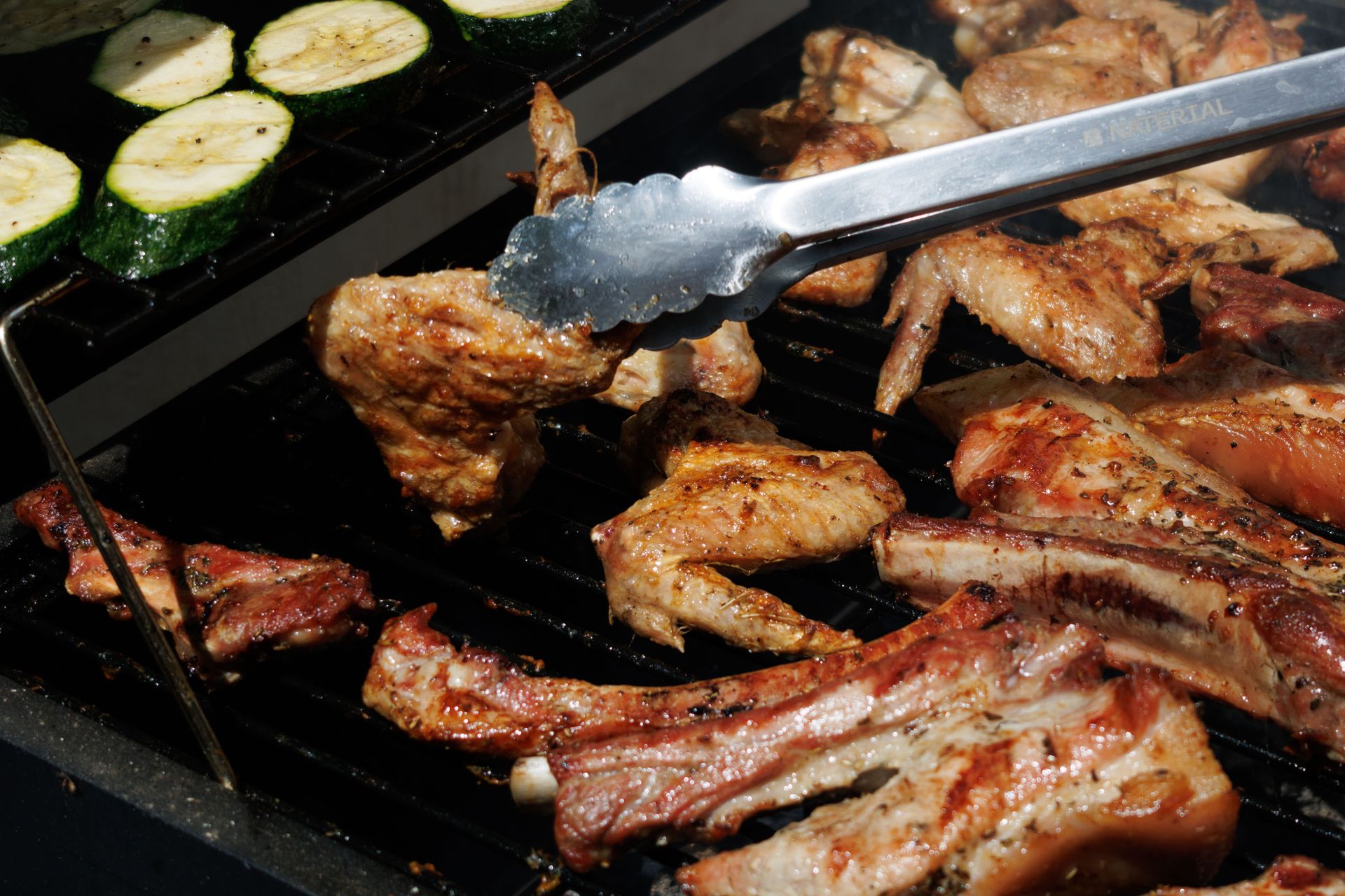 Juicy meat and zucchini being grilled on a barbecue under the summer sun.
