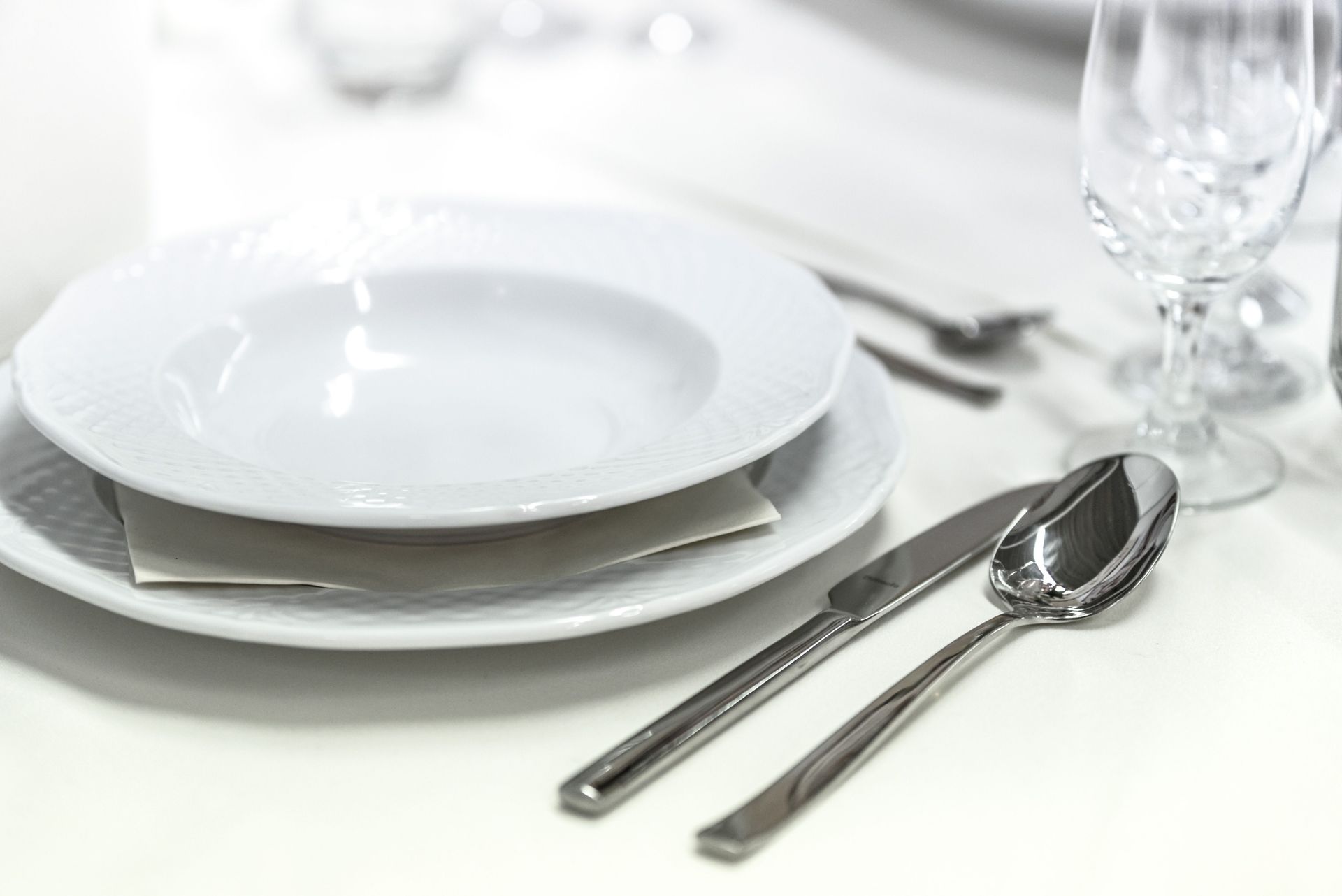 Elegant dining table with white porcelain plates and silver cutlery elegantly arranged.